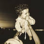 adult, arms, baby, chain, child, clothing, curly_hair, face, happy, holding, infant, night, outdoor, pacifier, person, playful, portrait, sepia, smiling, tattoo