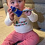 baby, child, onesie, christmas, toy_car, sitting, carpet, couch, striped_leggings, barefoot, playtime, indoor, cute, chewing, hands, portrait, floor, block_toy, happy, curious