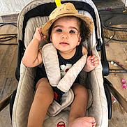 Danya participe au concours pour gagner de l'argent avec cette photo : toddler, child, stroller, hat, beige, floor, tiles, flower_petals, cables, curly_hair, cute, baby, foot, hand, clothing, seatbelt, indoor, portrait, casual, curious