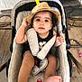 toddler, child, stroller, hat, beige, floor, tiles, flower_petals, cables, curly_hair, cute, baby, foot, hand, clothing, seatbelt, indoor, portrait, casual, curious
