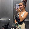 black_dog, buttons, casual_clothing, dog, earbuds, elevator, happy_dog, indoor, leash, metal_wall, mirror, phone, portrait, reflection, selfie, shorts, standing, tank_top, tattoos, woman