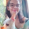 woman, dog, indoor, window, glasses, smile, pet, small_dog, collar, light, casual_clothing, tattoo, portrait, natural_light, curly_hair, white_dog, happy, looking_away, green_background, person