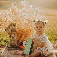 Zselyke joined the competition — help win amazing prizes! baby, child, outdoor, grass, flower_crown, book, basket, wooden_number, sunlight, field, dress, pigtails, woven_mat, nature, portrait, cute, sitting, daylight, infant, decor