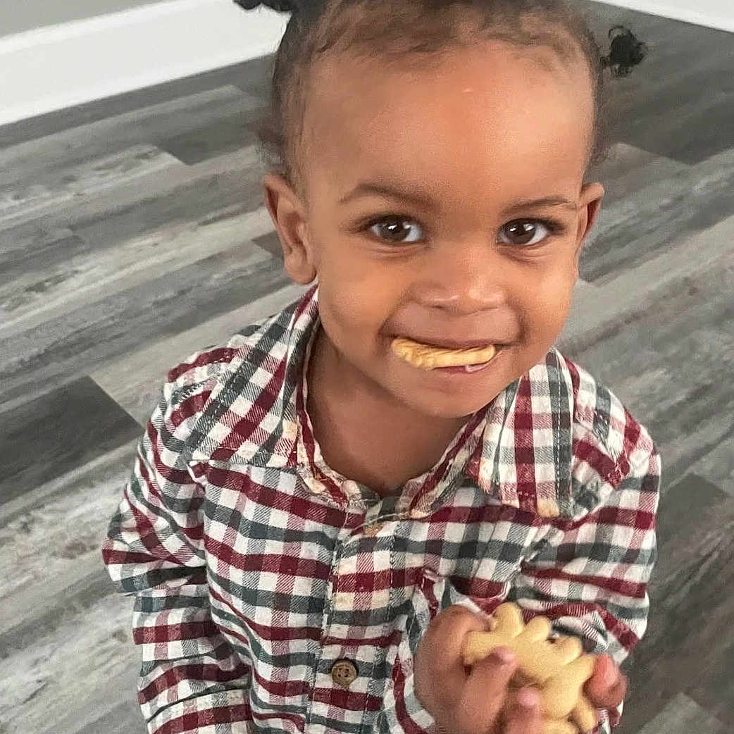 Demik joined the competition — help win amazing prizes! child, toddler, smiling, animal_crackers, food, snack, plaid_shirt, pigtails, hair, floor, wooden_floor, indoor, person, cute, happy, holding, standing, face, eyes, mouth