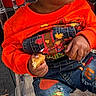 Demik is registered to the contest to win money with this photo: toddler, child, orange_beanie, orange_sweater, denim_jeans, colorful_patches, scarecrow_patch, smores_patch, snack, transparent_chair, outdoor, sitting, cute, curious_expression, casual_clothing, young_child, fashion, playful, portrait, daylight