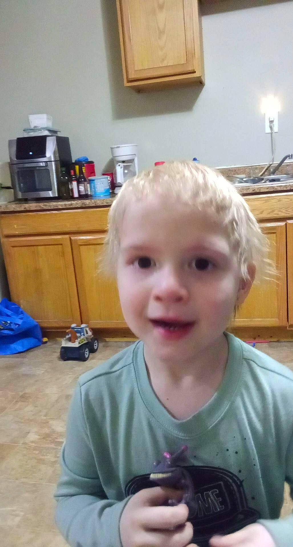 Abel is registered to the contest to win money with this photo: baby_toddler_clothing, bag, blue, cabinetry, candle, cheek, child, flooring, fun, head, home_appliance, joy, kitchen_appliance, light_fixture, luggage_and_bags, person, picture_frame, room, sitting, smile