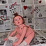 baby, infant, child, sitting, newspaper_backdrop, hearts, red_graffiti, crossword_puzzles, pink_overall, white_socks, tuft_hair, looking_up, portrait, indoor, staged_shot, playful, floor_covering, love_text, xoxo, cute