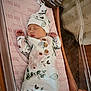 newborn, baby, sleeping, floral_clothing, hat, hospital_bassinet, pink_sheet, birth_announcement, wooden_sign, infant, peaceful, cute, portrait, indoors, person, child, baby_girl, resting, soft_lighting, hospital