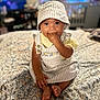 baby, bedspread, casual, child, cute, fabric, foot, furniture, hand_in_mouth, hat, indoor, infant, pattern, person, portrait, room, sitting, soft_light, striped_clothing, young_child
