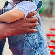 Kairo is registered to the contest to win money with this photo: baby, background_blur, candid, casual_clothing, child, curious, cute, daylight, denim_overalls, hand, holding, outdoor, person, portrait, red_chair, skin, standing, toddler, urban, white_socks