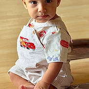 Kairo is registered to the contest to win money with this photo: toddler, child, baby, sitting, indoor, overalls, lightning_mcqueen, foot, hand, curious, expression, floor, cushion, pattern, clothing, person, portrait, cute, toy_car, young_child