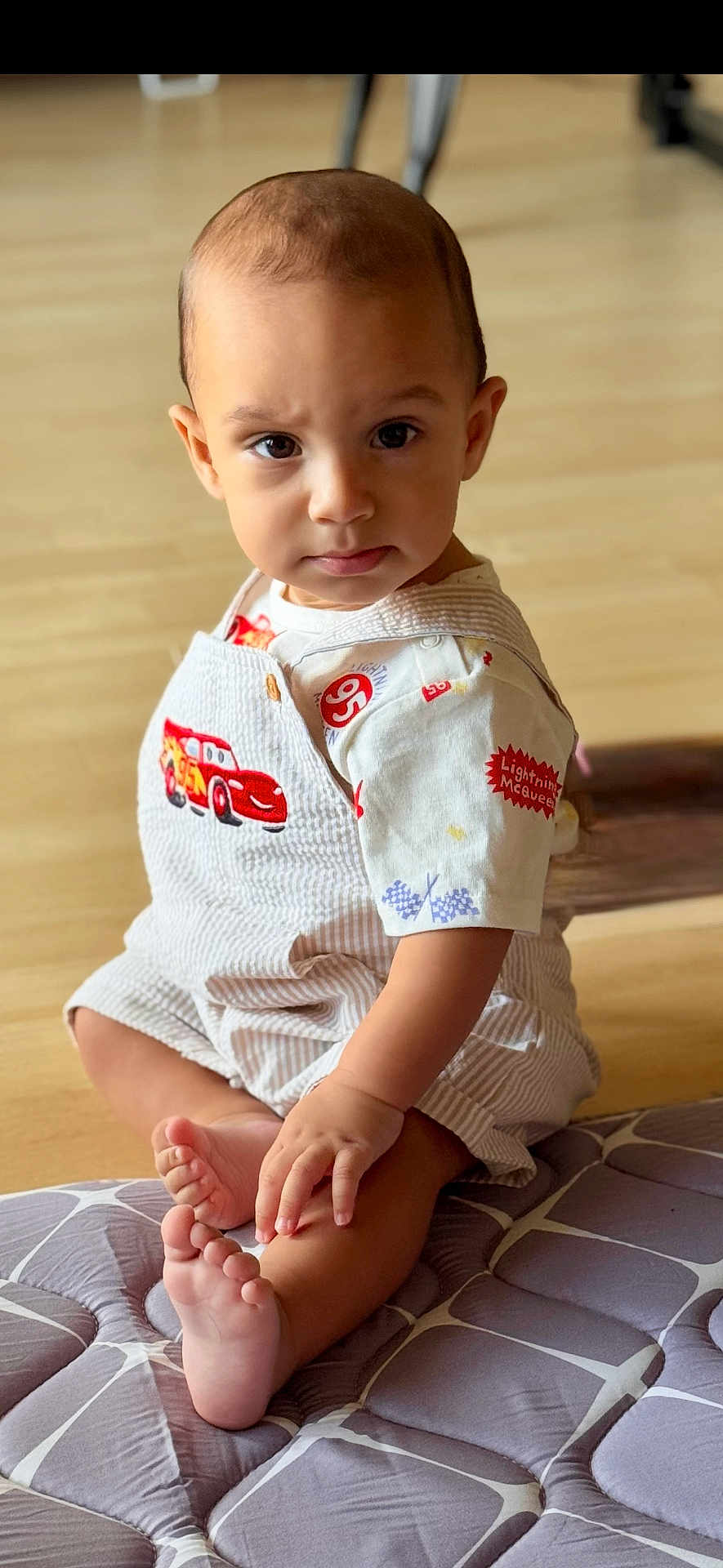 Kairo is registered to the contest to win money with this photo: toddler, child, baby, sitting, indoor, overalls, lightning_mcqueen, foot, hand, curious, expression, floor, cushion, pattern, clothing, person, portrait, cute, toy_car, young_child