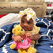 Tru joined the competition — help win amazing prizes! baby, child, teddy_bear, plush_toy, headwrap, blanket, bedroom, furniture, dresser, smiling, cute, indoors, clothing, infant, person, comfort, soft_toy, patterned, yellow, pink