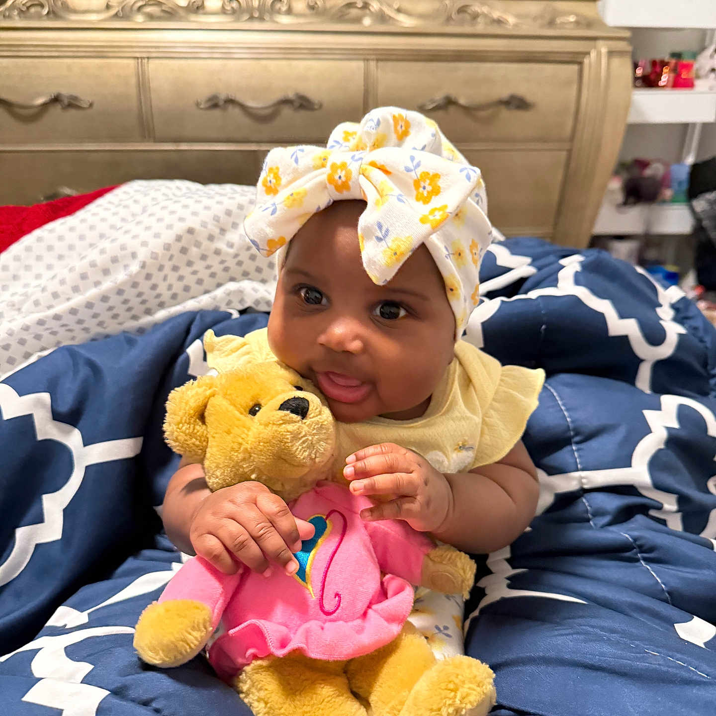 Tru joined the competition — help win amazing prizes! baby, child, teddy_bear, plush_toy, headwrap, blanket, bedroom, furniture, dresser, smiling, cute, indoors, clothing, infant, person, comfort, soft_toy, patterned, yellow, pink