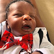 Elijah is registered to the contest to win money with this photo: baby, infant, face, expression, bow_tie, clothing, skin, hand, curly_hair, close_up, portrait, newborn, cute, child, person, white_shirt, indoor, soft_light, relaxed, young