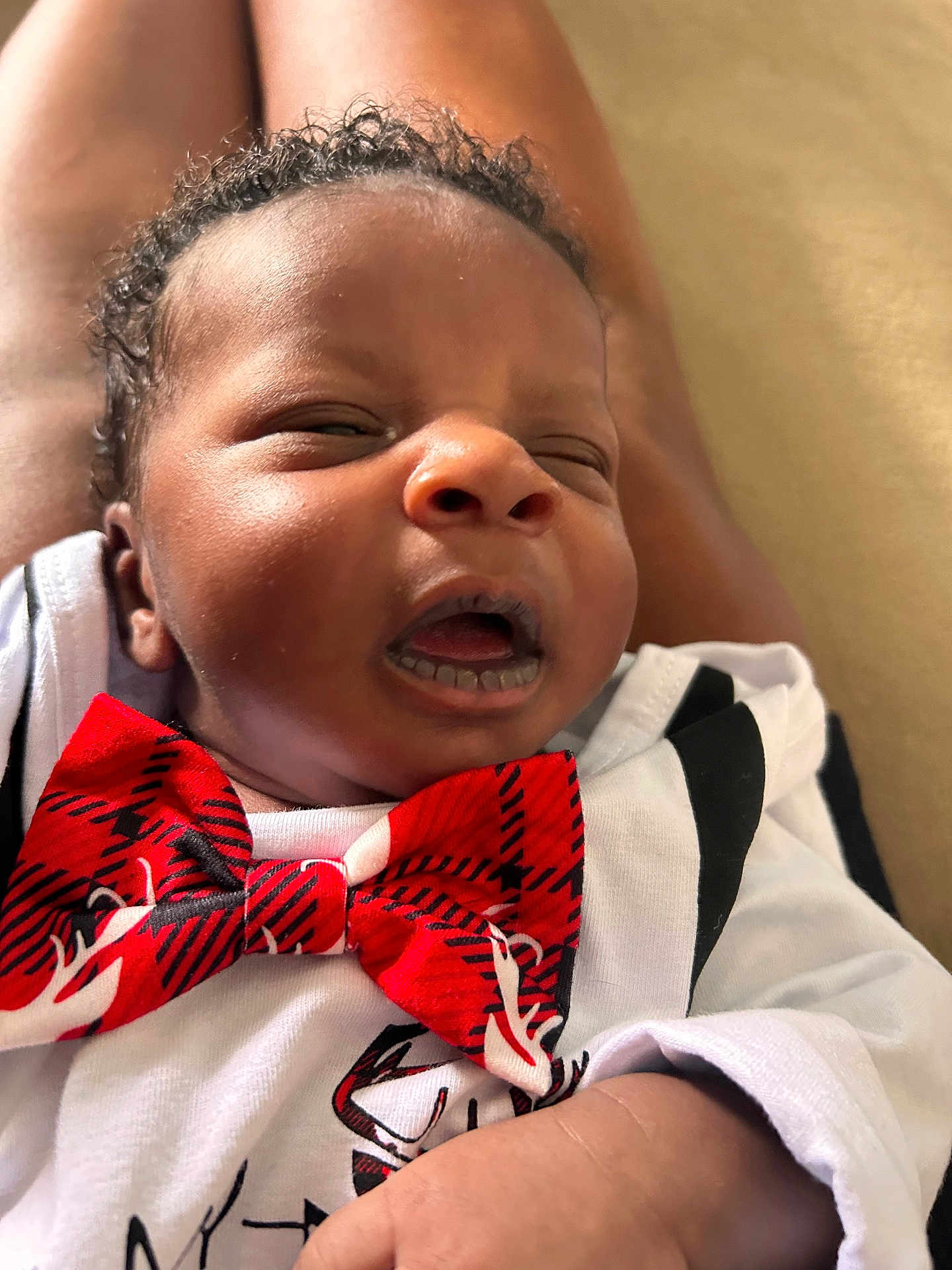 Elijah is registered to the contest to win money with this photo: baby, infant, face, expression, bow_tie, clothing, skin, hand, curly_hair, close_up, portrait, newborn, cute, child, person, white_shirt, indoor, soft_light, relaxed, young