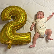 Ryta participe au concours pour gagner de l'argent avec cette photo : baby, infant, balloon, number_two, white_sheet, smiling, lying_down, celebration, chubby, cute, clothing, diaper, happy, gold, inflatable, party, child, face, skin, limbs