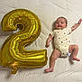 baby, infant, balloon, number_two, white_sheet, smiling, lying_down, celebration, chubby, cute, clothing, diaper, happy, gold, inflatable, party, child, face, skin, limbs