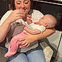 woman, baby, holding, kitchen, refrigerator, photos, oven, smiling, jeans, white_shirt, pink_pants, chair, floor, home_interior, appliance, family, indoor, person, tender_moment, seated