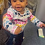 Alayah joined the competition — help win amazing prizes! toddler, child, smiling, indoor, colorful_clothing, heart_pattern, hair_clips, white_shoes, carpet, supporting_hand, person, cute, happy, young_child, standing, casual_wear, curly_hair, playful, home, baby