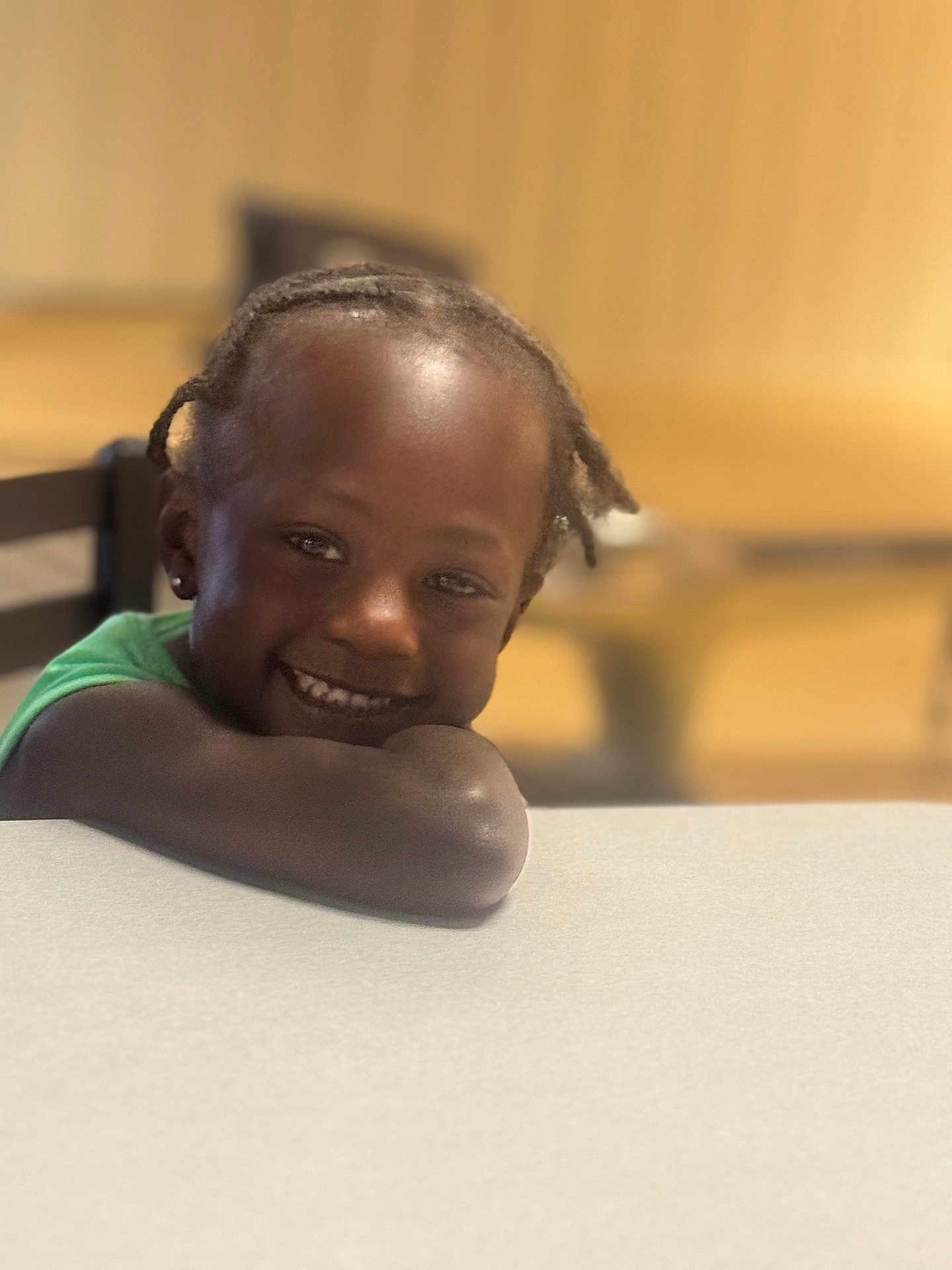 Kahmani joined the competition — help win amazing prizes! child, smile, happy, portrait, braided_hair, table, indoor, person, face, young, cute, resting, leaning, casual, joyful, head, skin, arm, seated, background_blur