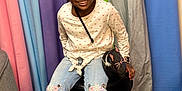 Khalani is registered to the contest to win money with this photo: child, girl, smiling, sitting, stool, jeans, shirt, hairstyle, braids, colorful_background, fabric, footwear, sneakers, purse, accessory, happy, portrait, indoor, playful, casual
