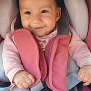 Camila is registered to the contest to win money with this photo: baby, child, car_seat, smile, pink, infant, seatbelt, clothing, cute, safety, happy, portrait, young_child, baby_girl, head, person, seat, straps, child_safety, indoors