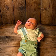 Draxton is registered to the contest to win money with this photo: baby, baby_clothing, child, cute, expression, eyes, face, green_suspender, hand, indoor, infant, laying_down, natural_light, newborn, portrait, skin, small, white_shirt, wood_texture, wooden_floor