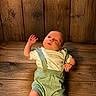 baby, baby_clothing, child, cute, expression, eyes, face, green_suspender, hand, indoor, infant, laying_down, natural_light, newborn, portrait, skin, small, white_shirt, wood_texture, wooden_floor
