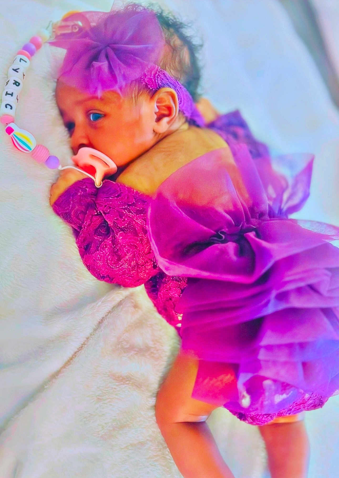 Lyric is registered to the contest to win money with this photo: baby, infant, purple_dress, bow, pacifier, beaded_clip, blanket, lying_down, cute, newborn, soft_texture, face, headband, sleepy, child, adorable, indoors, closeup, person, toddler