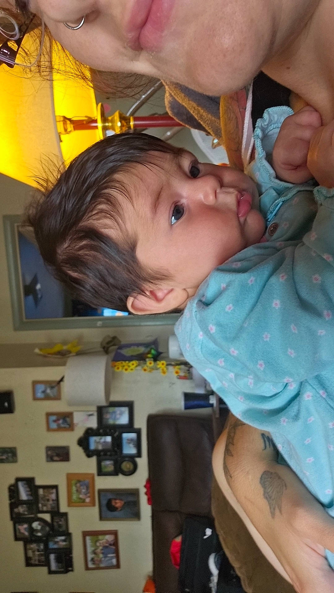 adult, baby, blue_clothing, child, closeup, couch, cozy, curious, face, hair, holding, home, indoor, infant, lamp, living_room, person, picture_frames, skin, tattoo