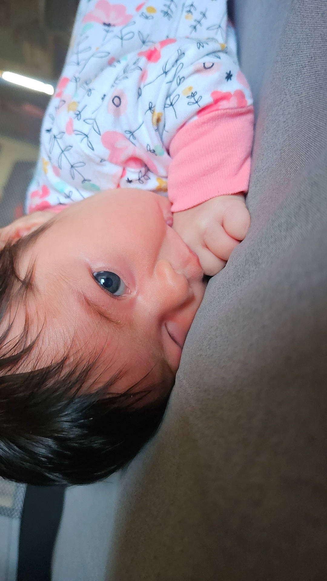 baby, blue_eyes, child, closeup, cute, dark_hair, face, floral_clothing, hand, indoors, infant, lying_down, person, portrait, skin, sleepwear, sleeve, soft_surface, thumb, young