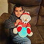 child, boy, smiling, plush_toy, snowman, glowing_ball, red_and_white, striped_sweater, striped_hat, jeans, jacket, indoor, couch, brown_couch, seated, cozy, happy, portrait, casual_clothing, home