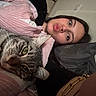 person, cat, tabby_cat, selfie, bed, pillow, blanket, indoor, cozy, face, pout, snuggling, resting, striped_blanket, green_eyes, long_hair, bracelet, nose_ring, casual, relaxed