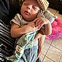 baby, sleeping, hat, stuffed_animal, blanket, person, hand, clothing, indoor, floor_tiles, couch, pink_pillow, gray_pants, toddler, cute, peaceful, infant, child, holding, relaxing