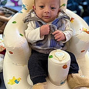 Matteo is registered to the contest to win money with this photo: baby, infant, child, vest, knitted_booties, inflatable_chair, clothing, sitting, indoor, face, hand, zipped_jacket, comfort, cute, colorful, background_blur, expression, person, young, cozy