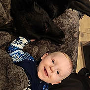 Liam participe au concours pour gagner de l'argent avec cette photo : baby, infant, smiling_baby, black_dog, dog, pet, cuddling, blanket, fur, cozy, indoors, pajamas, blue_pattern, face, portrait, lying_down, home, cute, playful, companion