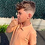 Lyham participe au concours pour gagner de l'argent avec cette photo : boy, child, outdoor, daylight, holding_bottle, orange_cap, peach_shirt, short_sleeves, curly_hair, side_profile, fence, concrete_wall, shadow, pavement, thinking, casual_clothing, summer, person, standing, sunlight
