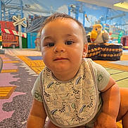 Wyatt is registered to the contest to win money with this photo: animal_print, baby, background, bib, bird_figure, carpet, child, colorful, cute, expression, floor, indoor, infant, mural, pattern, play_area, playground, portrait, seated, toy