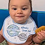 baby, background, bib, child, clothing, cute, diaper, expression, face, food, hand, happy, indoor, infant, person, short_hair, sitting, skin, smile, snack