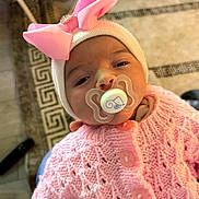 Larissa joined the competition — help win amazing prizes! baby, pacifier, pink_bow, knitted_sweater, hat, infant, child, cozy, cute, indoors, person, portrait, hand, patterned_rug, home, soft_lighting, close_up, newborn, sleepy, warm