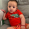 Jake joined the competition — help win amazing prizes! baby, child, infant, cute, dinosaur_shirt, orange_shorts, sitting, gray_chair, indoor, relaxed, portrait, young_child, casual_clothing, barefoot, bracelet, curly_hair, expression, small_hand, comfort, looking_at_camera