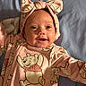 Hazel joined the competition — help win amazing prizes! baby, infant, child, portrait, smiling, happy, face, headband, bow, pink_clothing, onesie, winnie_the_pooh, cartoon_character, lying_down, indoors, blanket, bed, close_up, front_view, cute