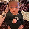Hazel joined the competition — help win amazing prizes! baby, infant, child, portrait, sitting, wide_eyed, serious_expression, black_onesie, clothing, bed, blanket, cushion, tattooed_arm, adult_hand, indoors, bedroom, close_up, face, photography, safe