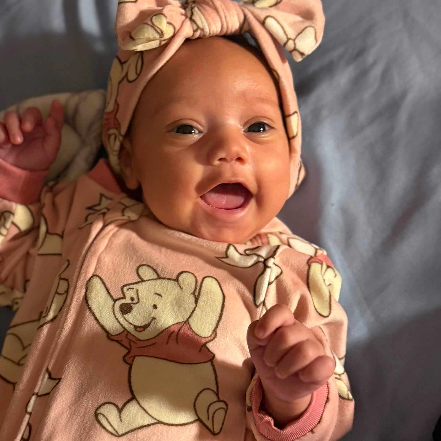 Hazel joined the competition — help win amazing prizes! baby, infant, child, portrait, smiling, happy, pink_outfit, headband, bow, winnie_the_pooh, cartoon_character, lying_down, blanket, bed, indoors, close_up, face, hands, fashion, cute