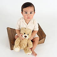 Liam joined the competition — help win amazing prizes! toddler, child, teddy_bear, plush_toy, wooden_crate, white_background, sitting, portrait, cute, serious_expression, indoors, soft_lighting, barefoot, short_sleeves, brown_hair, large_eyes, studio_photo, holding, toy, young_child