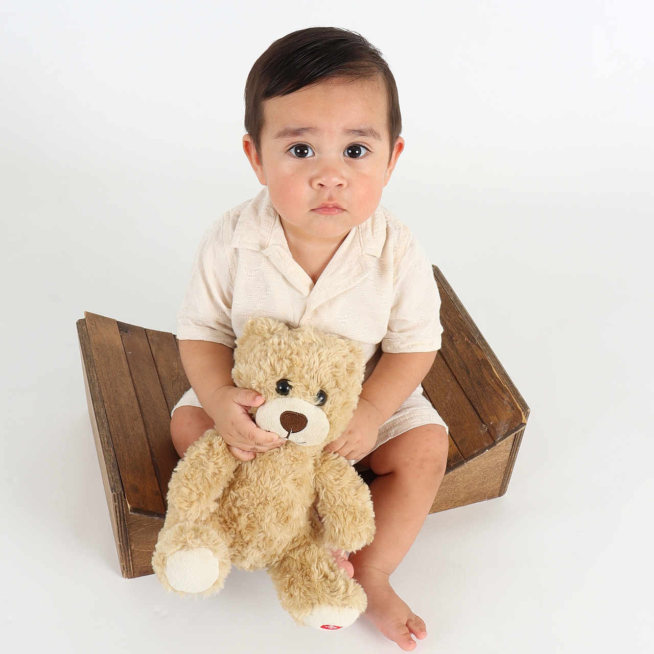 Liam joined the competition — help win amazing prizes! barefoot, brown_hair, child, cute, holding, indoors, large_eyes, plush_toy, portrait, serious_expression, short_sleeves, sitting, soft_lighting, studio_photo, teddy_bear, toddler, toy, white_background, wooden_crate, young_child