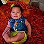 baby, child, clothing, cute, denim_vest, flower_clip, foot, hand, happy, indoor, infant, orange_blanket, patterned_blanket, person, portrait, skin, smiling, white_flower, wicker_basket, yellow_shorts