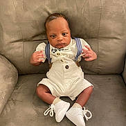 Roman is registered to the contest to win money with this photo: baby, infant, sitting, white_clothing, suspenders, bow_tie, white_shoes, couch, furniture, indoor, cute, child, portrait, small_hands, curious, young, person, fashion, comfortable, home