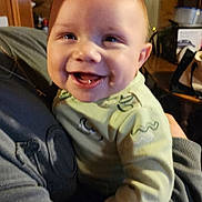 Armani is registered to the contest to win money with this photo: baby, smile, happy, child, person, indoor, clothing, holding, face, cute, young, infant, apparel, pattern, room, furniture, wood, portrait, warm, family